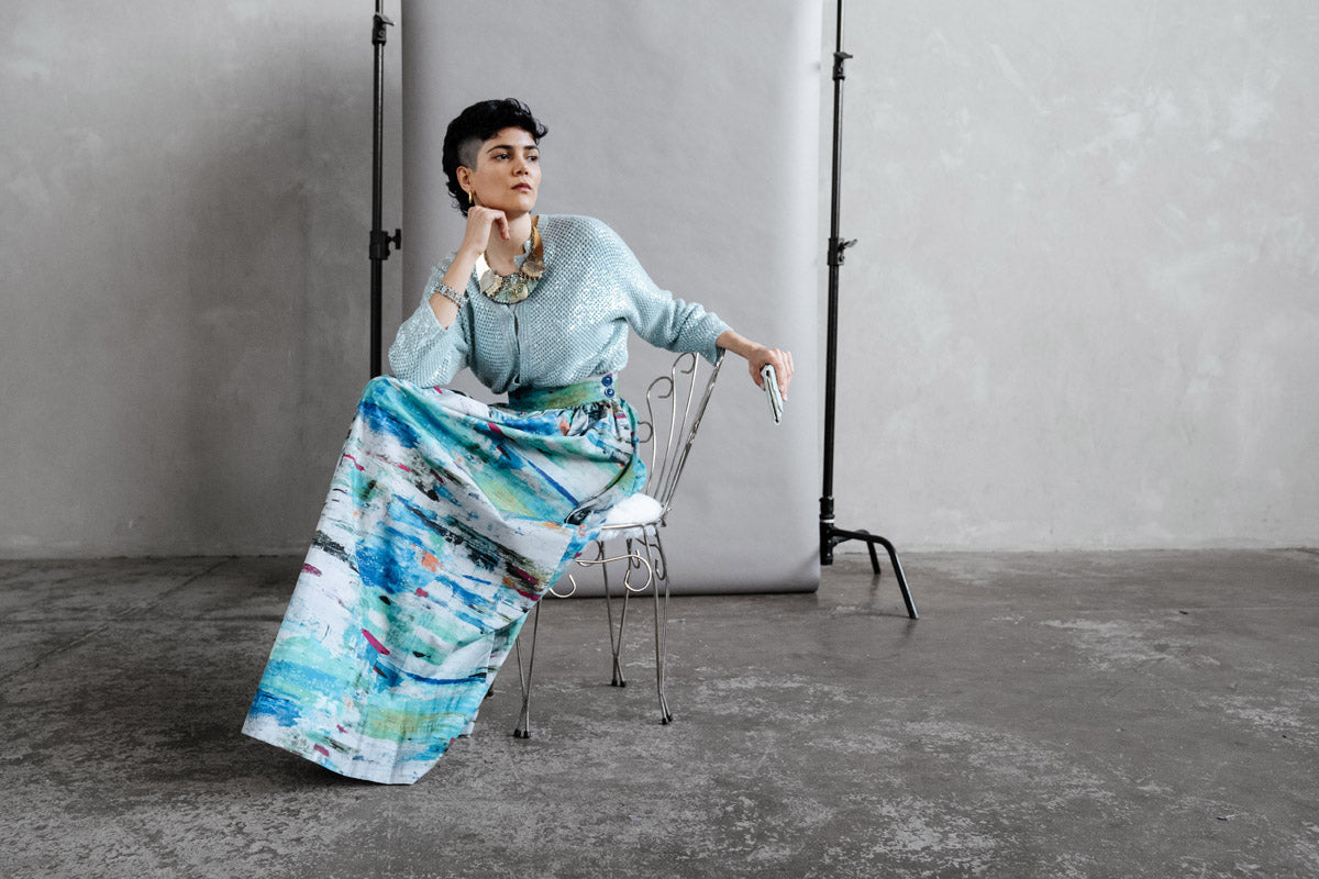 Model wears a by Audrey & Grace full length Ocean Skirt, with wide waist band and large hidden pockets. The print is a stunning abstract print of blues and greys with a hint of orange, black and fuscia. Crisp, comfortable made from organic cotton.