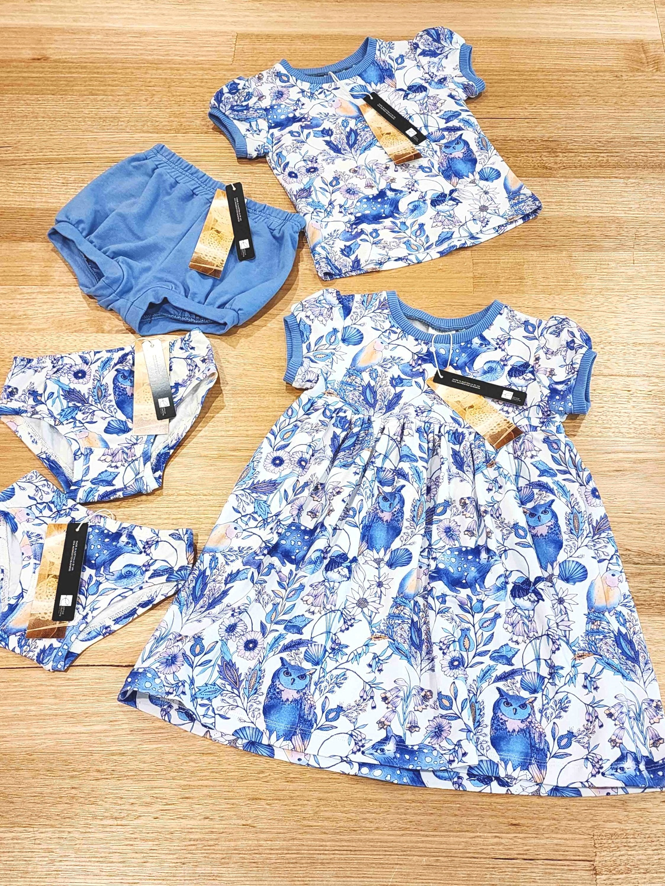 Flat Lay of new childrens collection featuring girls dresses, kids tees and bloomers in two colour ways, Owl and Quoll in white an Blue and Magnetic in bright multi colours featuring fuscia trim