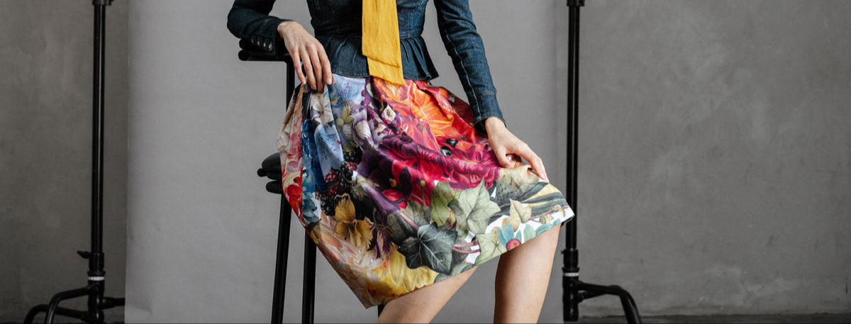 by Audrey & Grace Box Pleat Zero Waste skity with big Bold flowers worn by model, sitting on stool showing drape and the print.
