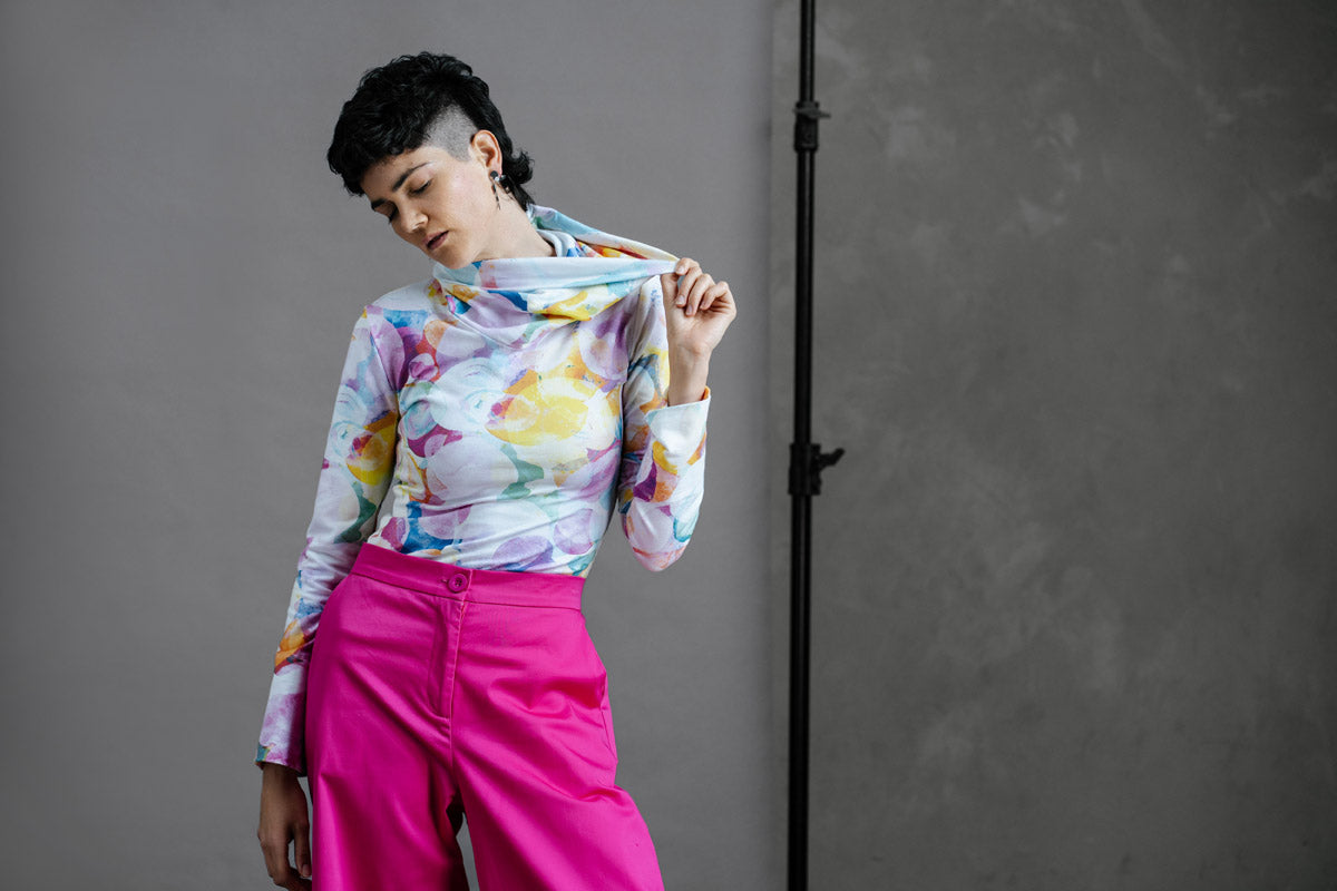 Model in by Audrey & Grace Ruby Jumper in Bubbles print, stretching out the large, cosy turtleneck, paired with thrifted, high waisted bright pink trousers.