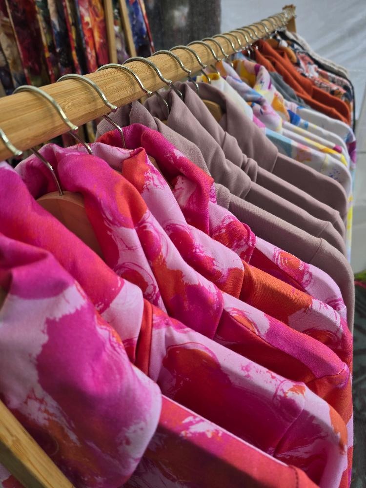 A wooden rack can be see on a slight angle from front to back. The ruby jumper Fairy flossis at the front and we can see the folded over cowl turtle neck and shoulder of 5 of these then we can see the lavender jumpers in the ruby jumper style and then some more, getting smaller as the image moves further away