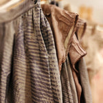 Zero Waste Skirt Gathered Abstract in blue grey abstract wave print seen with aero waste tops antique hanging on wooden hangers on a wooden rack. most of the image is in soft focus with the side pocket in focus