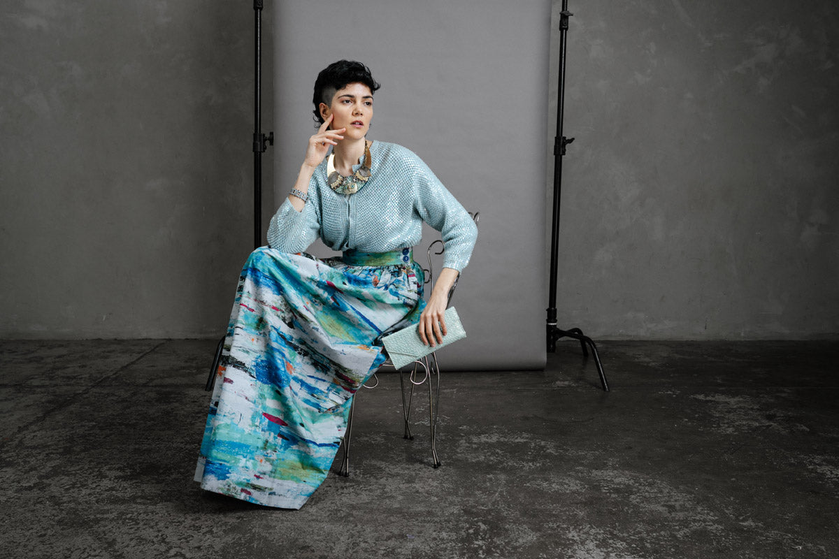 The by AUdrey and Grace Zero Waste Skirt in Ocean print, worn seated and full length with gathered waste.  Styled with a thrifted pale blue sequined cardigan and pale blue clutch.