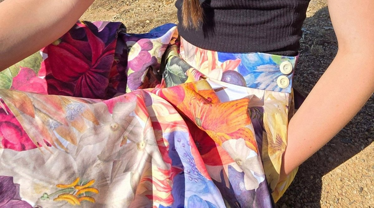 model wearing the Zero Waste Big Bloom Box Pleat Skirt, sitting on ground, with the organic cotton skirt softly folding over legs and left hand in the large side pocket