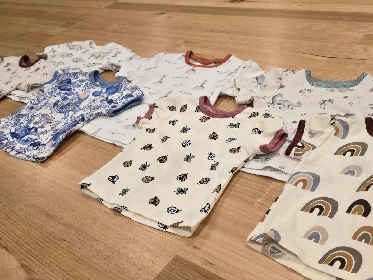 a collection of by Audrey and Grace Australian made kids tees laying on top of one another on a wooden table. Prints include; rainbows, ladybigs, owl and quoll, turtles, lighthouse and dinosaurs
