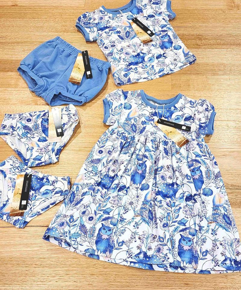 Flat Lay of new childrens collection featuring girls dresses, kids tees and bloomers in two colour ways, Owl and Quoll in white an Blue and Magnetic in bright multi colours featuring fuscia trim