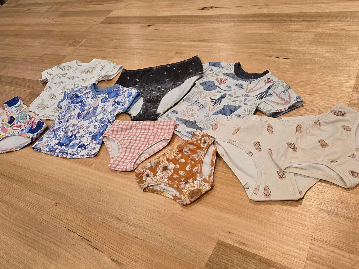 A selection of by Audrey and Grace gifts under $55 flat lay on wooden table including Australian made underwear and Australian made kids tees