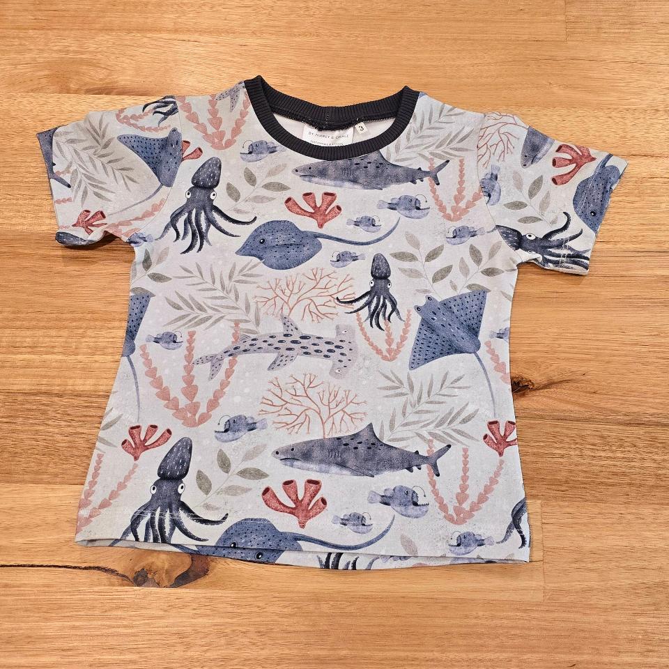 We can see a childs t shirt featuring an underwater scene print with stingray, squid, hammerhead shark and more