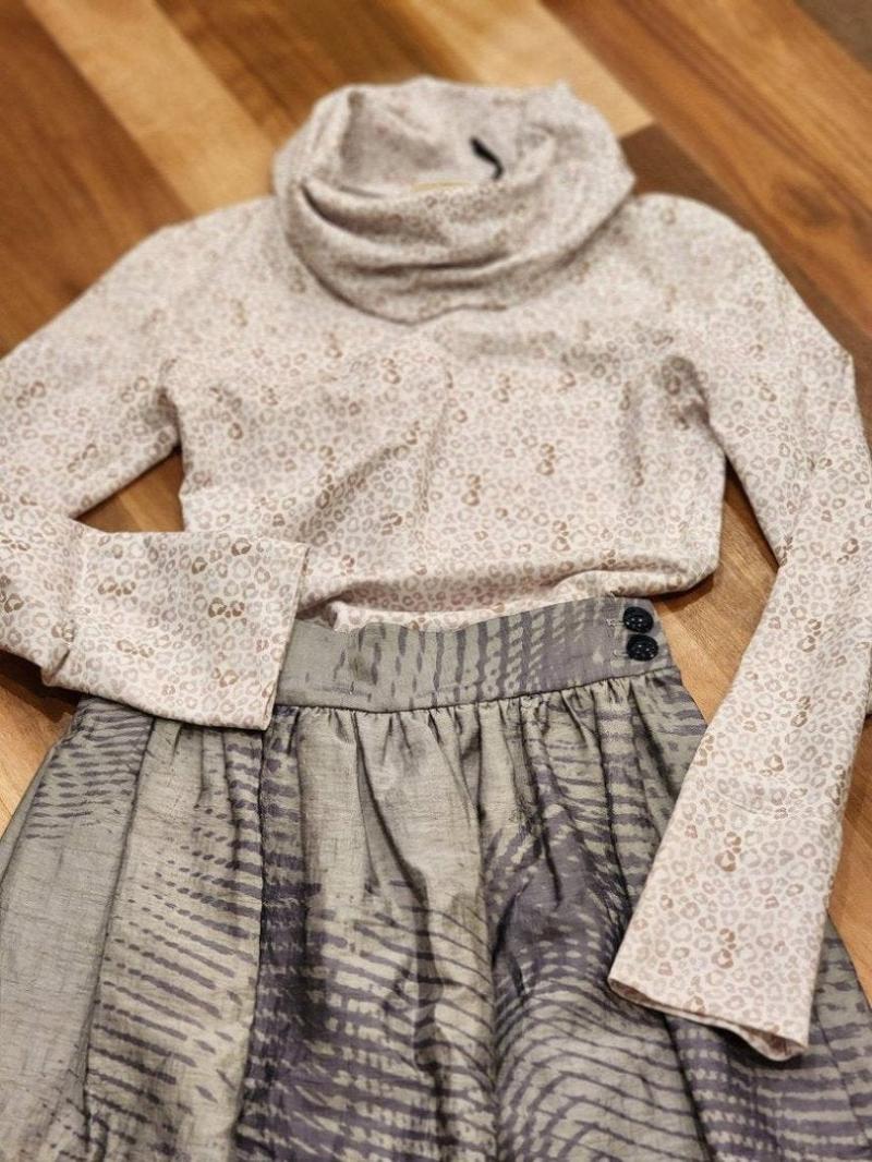 Zero Waste Skirt Gathered Abstract and Leopard print Ruby Jumper laying in a flat lay with the ruby jumper appearing to be tucked into the skirt with one arm bent and resting on the wide waistband of the skirt and the other sleeve laying over the skirt at the side pocket. Two deep blue vintage buttons can be seen on the waistband and the large cowl turtle neck collar of the ruby jumper is in soft focus