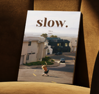 A copy of SLOW. magazine with a woman skating down a steep road on the cover. The magazine is on an armchair.