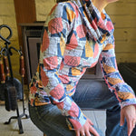 Model wears the Ruby Jumper in the Jumble print. Sitting side on , showing long boddy and long sleeves with foldable cuffs at full length and cowl turtle neck collar softly folding around neck