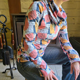 Model wears the Ruby Jumper in the Jumble print. Sitting side on , showing long boddy and long sleeves with foldable cuffs at full length and cowl turtle neck collar softly folding around neck