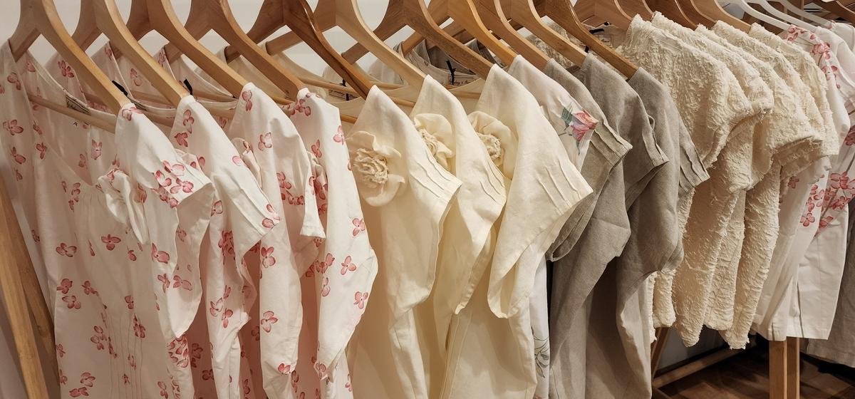 A rack with a variety of by Audrey & Grace Zero Waste tops hanging on wooden hangers