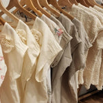 A row of by Audrey and Grace Zero Waste Tops in different shades and fabrics hanging on wooden hangers.