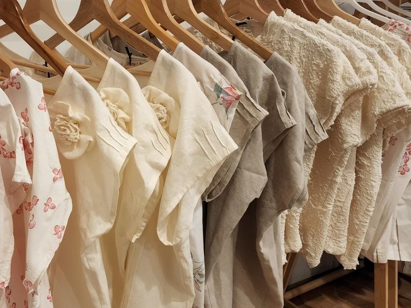 A row of by Audrey and Grace Zero Waste Tops in different shades and fabrics hanging on wooden hangers.