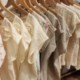 A selection of neutral coloured by Audrey And Grace Zero Waste tops hanging on a rack on wooden coathangers