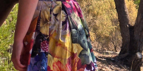 Model wearing the Big Bloom Box Pleat Skirt, side on with back showing and resting hand on a tree.  Wearing the hand crafted zero waste skirt with corozo buttons and accredited by Ethical Clothing Australia. A beautiful piece of Australian Made womens clothing.