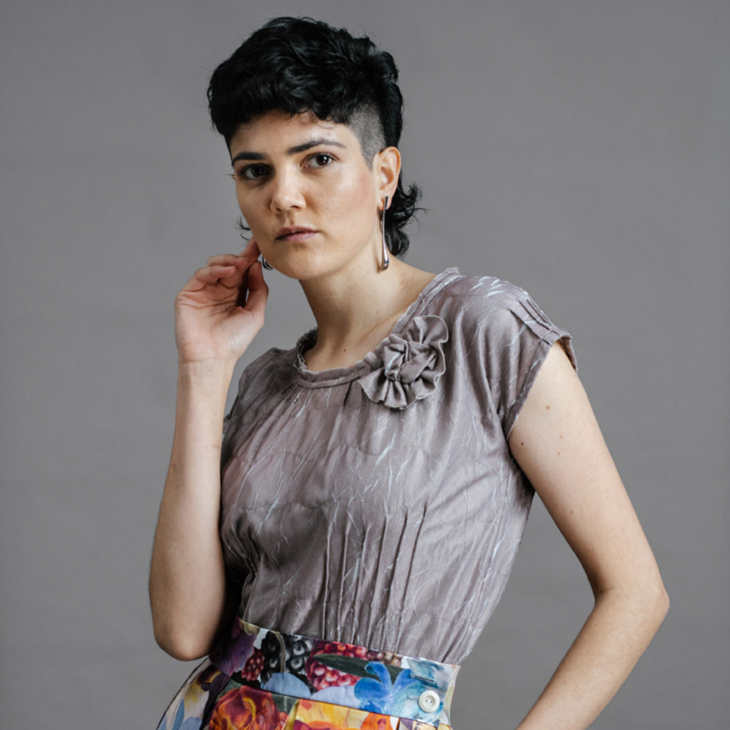 Model wearing the by Audrey and Grace Antique Zero Waste top. We can see the flower detail and the pin tucks and it is worn with the Big Bloom Zero Waste skirt. with models hand held up to face standing on a slight angle
