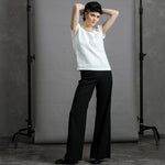 Full length image of a model wearing the by Audrey and Grace Oyster coloured zero waste top. Featuring pin tucks for elegance and shaping and rosette at shoulder.  The models hands are behind her head and the top sits at her hips. It is worn with grey wool pin stripe Australian made women's trousers.