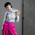 Model in by Audrey & Grace Ruby Jumper in Bubbles print, stretching out the large, cosy turtleneck, paired with thrifted, high waisted bright pink trousers.