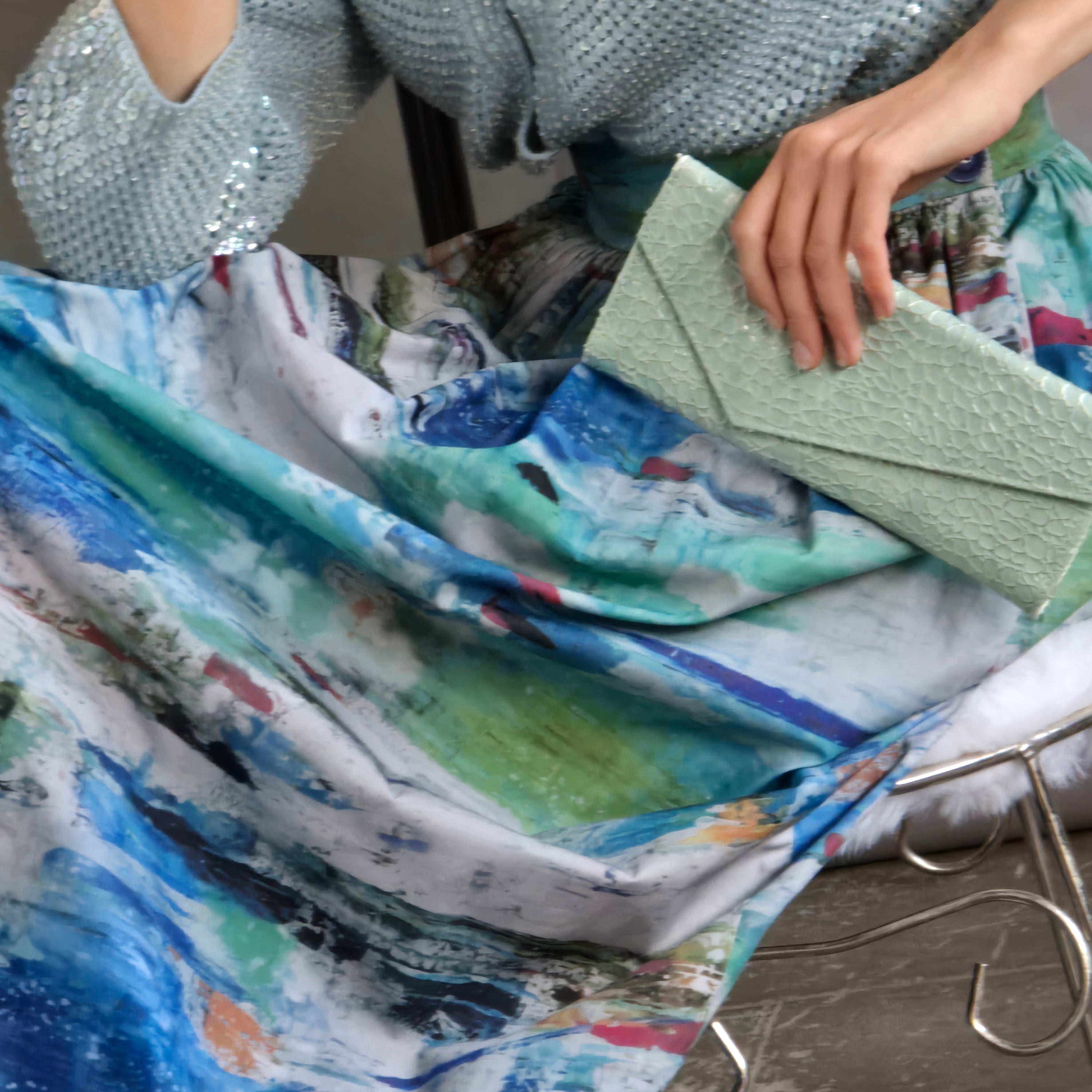Image of by Audrey and Grace Zero Waste full length Ocean Skirt, close up of model sitting on a vintage vanity chair, also wearing a thrifted, hand beaded dress cardigan and baby blue, with a blue sparkling vintage watch and a pale turquoise clutch.