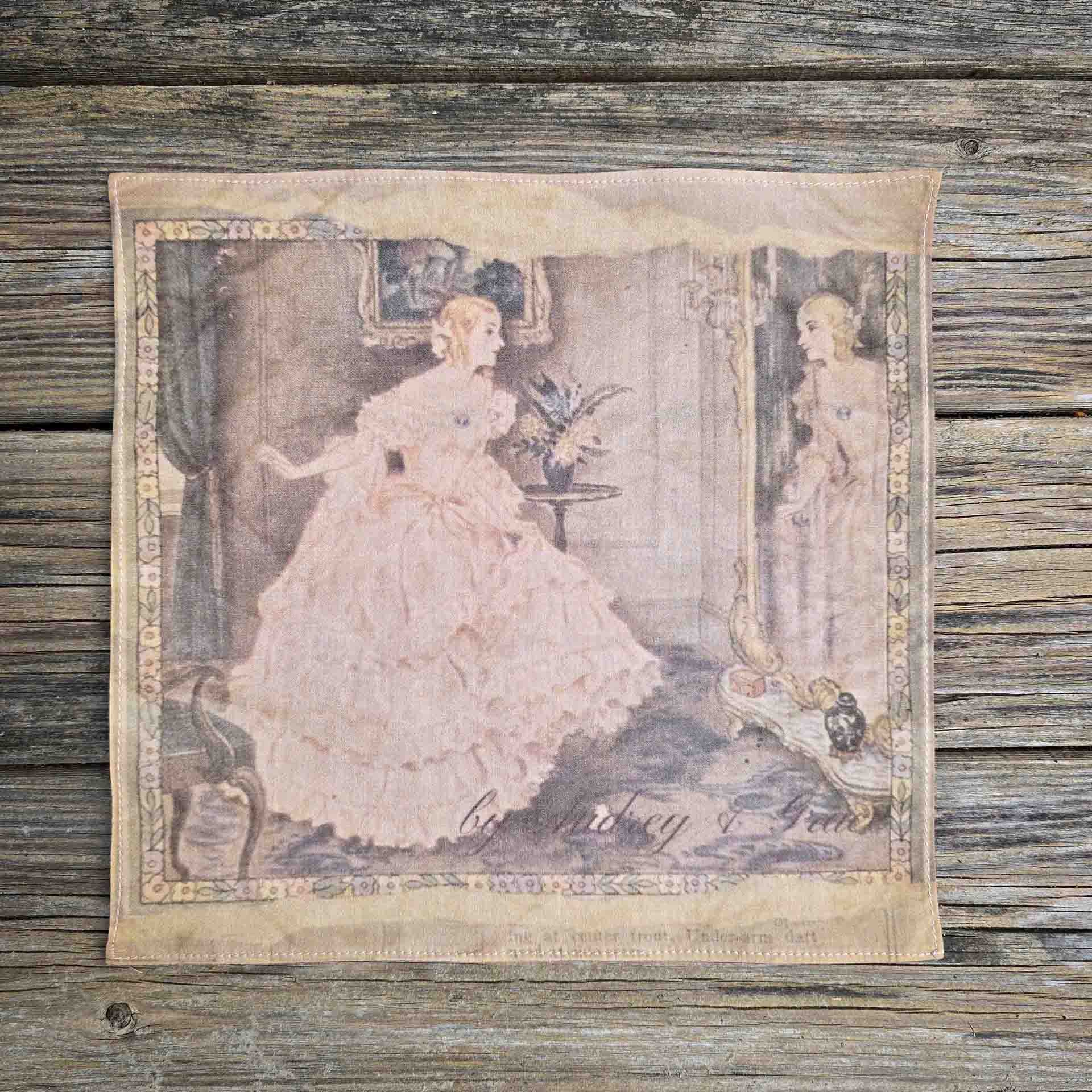 An image of a ladies handkerchief made from fine Pima Cotton Lawn. The print depicts a woman wearing a corseted gown with crinoline, lavished with a full pink gathered skirt, admiring herself in an ornate mirror.