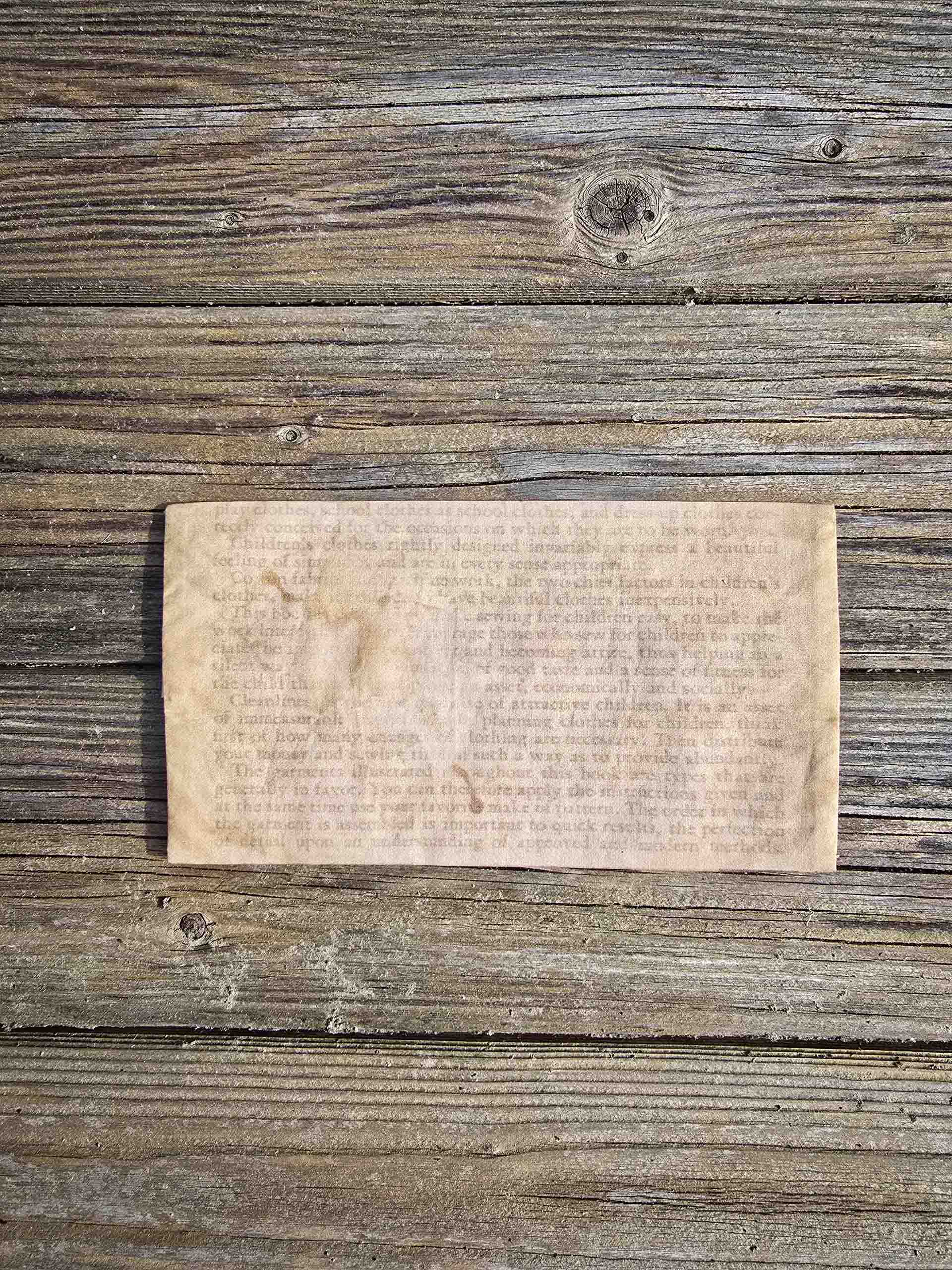 The back side of a delicate rectangular hanky pouch, showing text from a booklet, hard to read, aged with a coffee stain over the top of it.