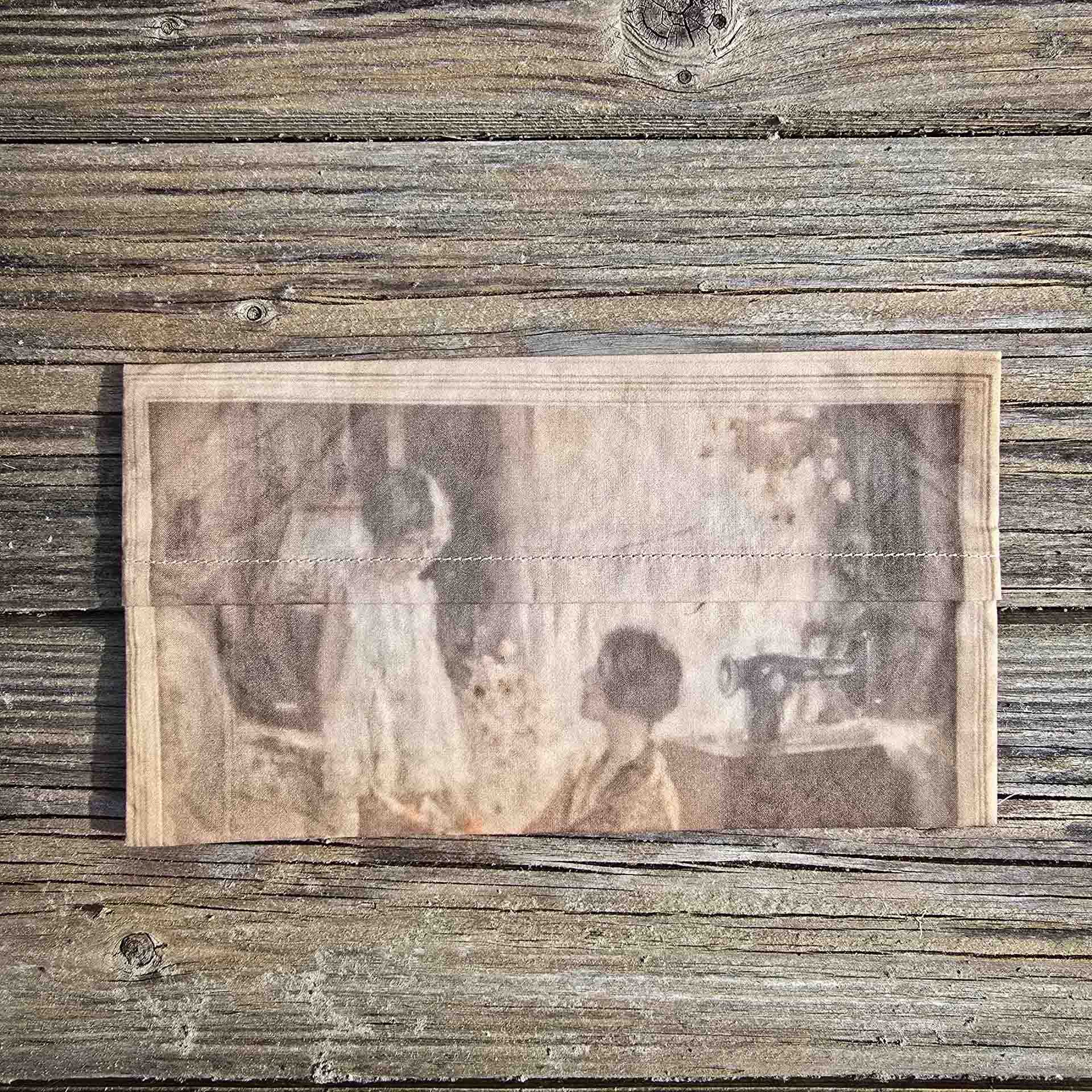 A small delicate rectangular pouch can be seen, with the image of a mother from the 1920s adjusting her little girls hem.