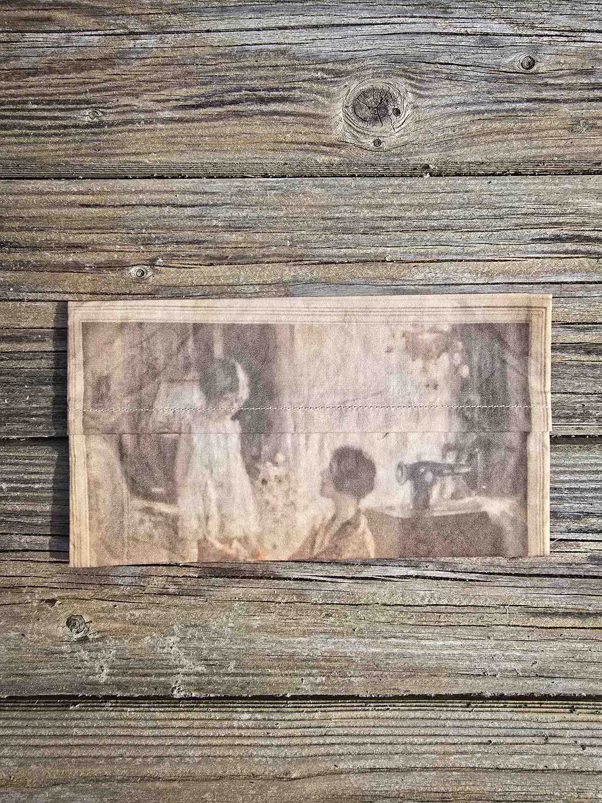 A small delicate rectangular pouch can be seen, with the image of a mother from the 1920s adjusting her little girls hem.
