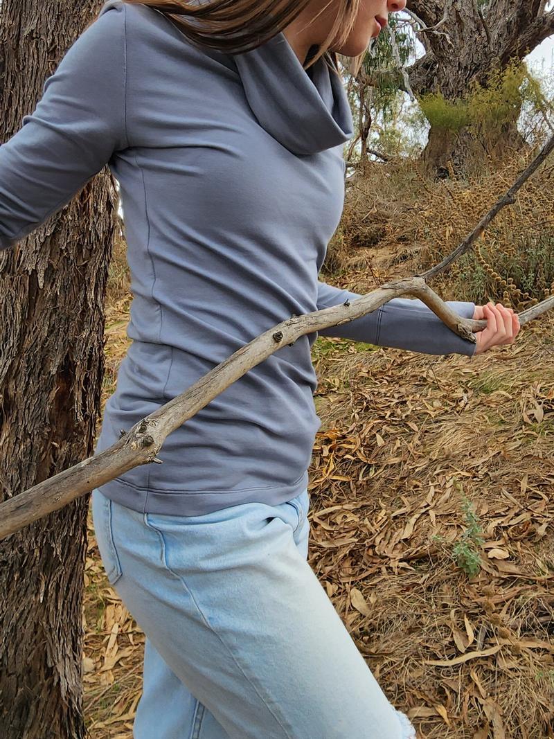 The Ruby Jumper in Storm, a blue grey colour, with large cowl neck, Australian Women's Jumpers made from Australian cotton — model side on walking through nature, cropped
