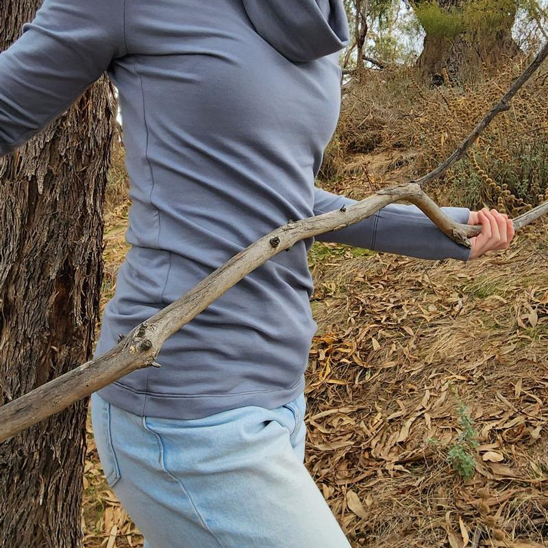 The Ruby Jumper in Storm, a blue grey colour, with large cowl neck, Australian Women's Jumpers made from Australian cotton — model side on walking through nature, cropped
