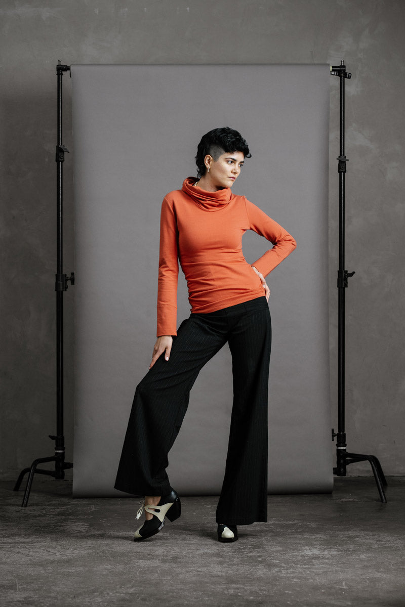 The Ruby Jumper in Terracotta, sustainable and ethical women's jumpers made from Australian cotton — front view with model's hand on hip and knee bent to the side, other hand on knee