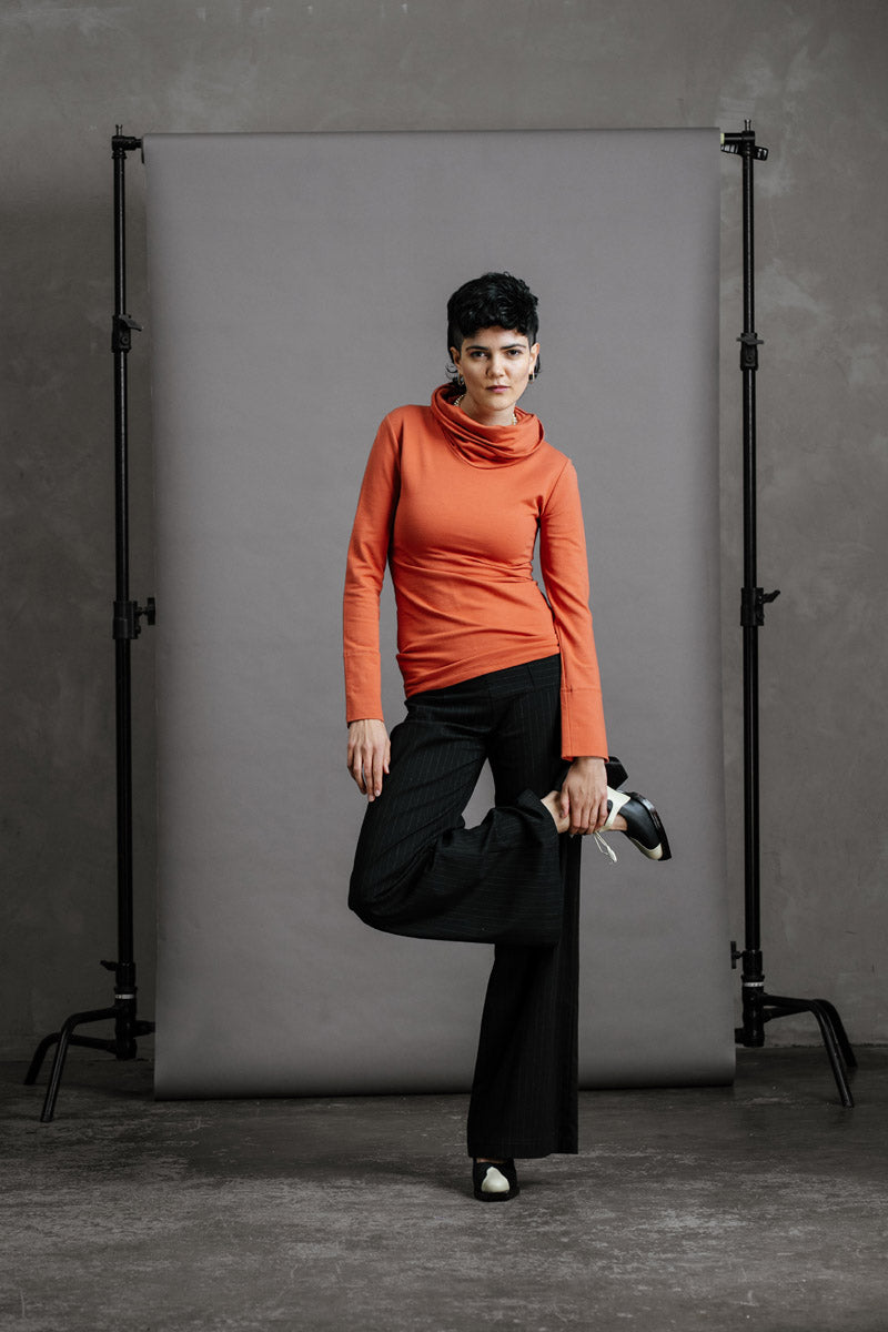 The Ruby Jumper in Terracotta, sustainable and ethical women's jumpers made from Australian cotton — front view, model holding foot with leg bent and foot at hip