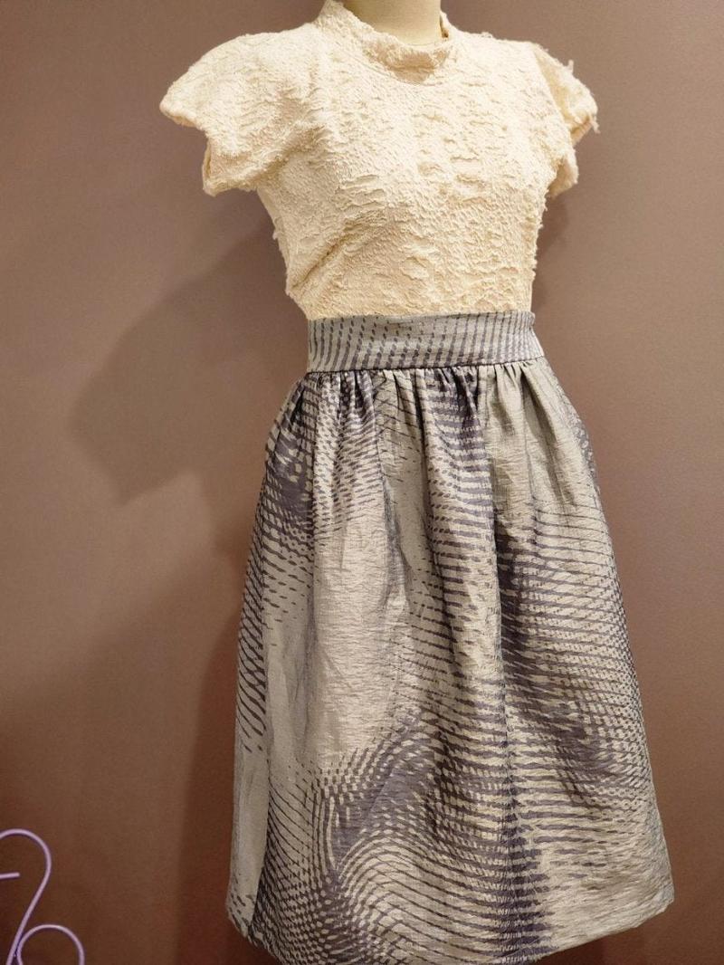 by Audrey and Grace zero waste skirt with an abstract wave print worn over a cream top and modelled on a mannequin. It is fitted at the waist and is a tailored skirt in a classic style with timeless design. the skirt sots just below knee height.